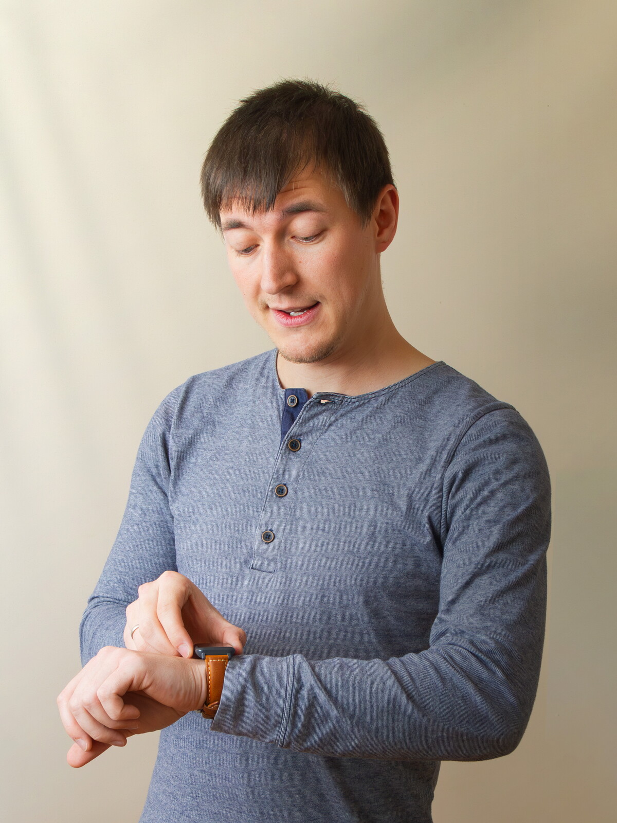 Julian im graublauen Langarmshirt blickt mit gespielt prüfendem Gesichtsausdruck auf seine Armbanduhr.