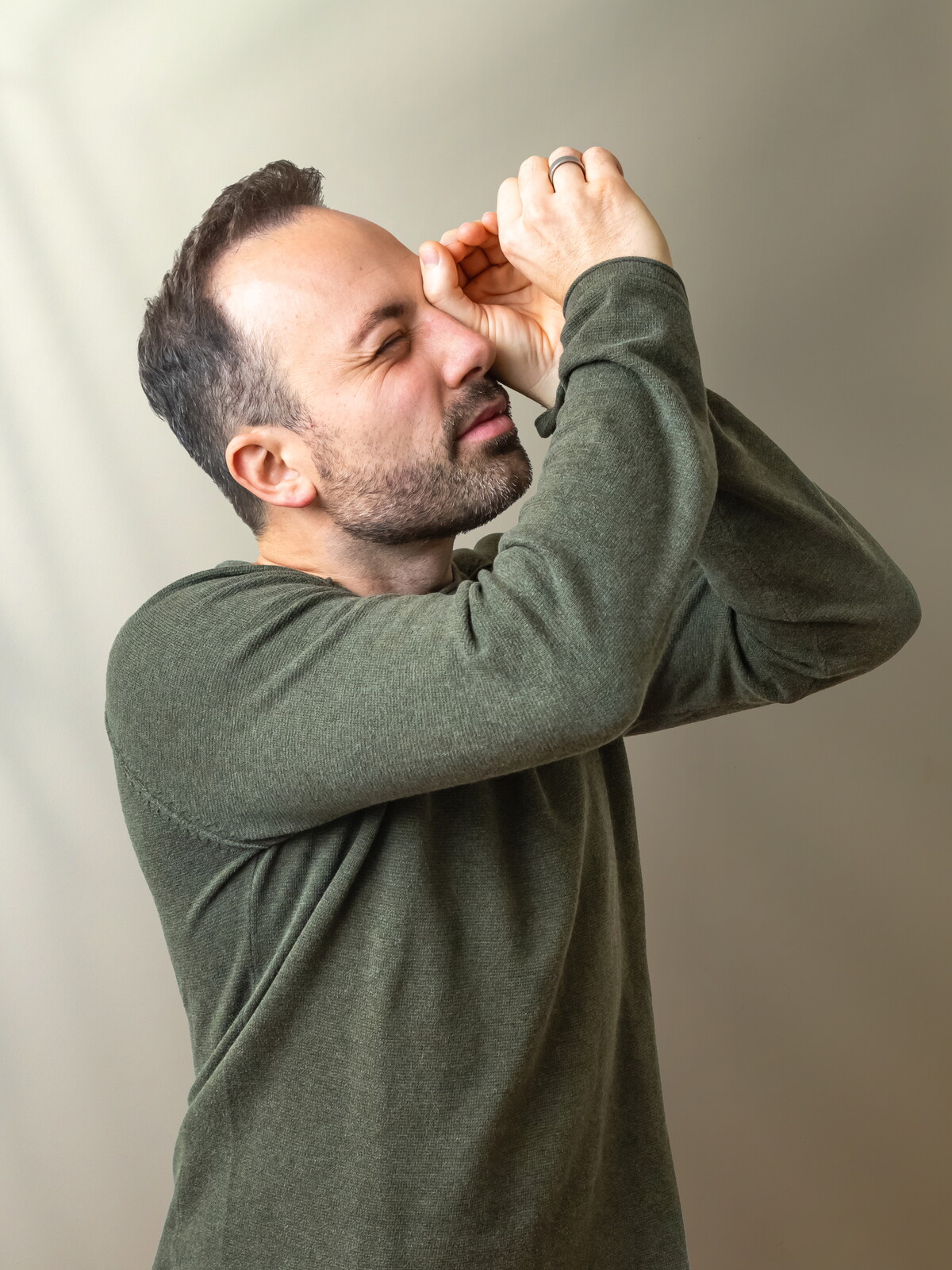 Christoph im olivgrünen Pullover formt mit den Händen ein Fernrohr vor dem Auge und hält schmunzelnd Ausschau.