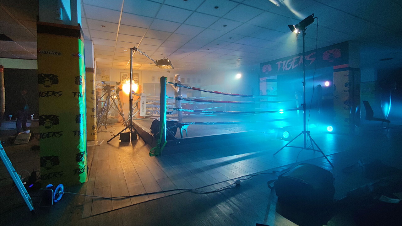 Filmset in einer Boxhalle: Ein Boxring ist in Nebel und blaues Scheinwerferlicht getaucht, davor stehen Leuchten und Technik auf dem Boden.