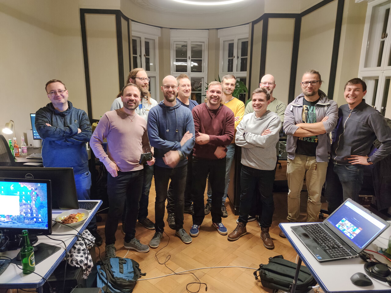 Gruppenfoto von zwölf Kollegen mit verschränkten Armen bei der POSTYOU-LAN-Party 2022. Sie stehen im Büro zwischen Tischen mit Laptops und Monitoren.