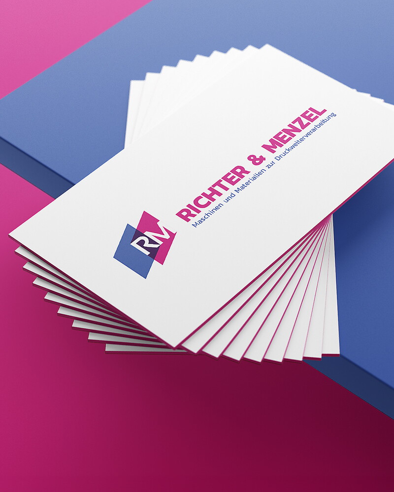Ein Fächer weißer Visitenkarten von Richter & Menzel mit pinker Kante und Logo liegt auf einem blau-pinken Untergrund.
