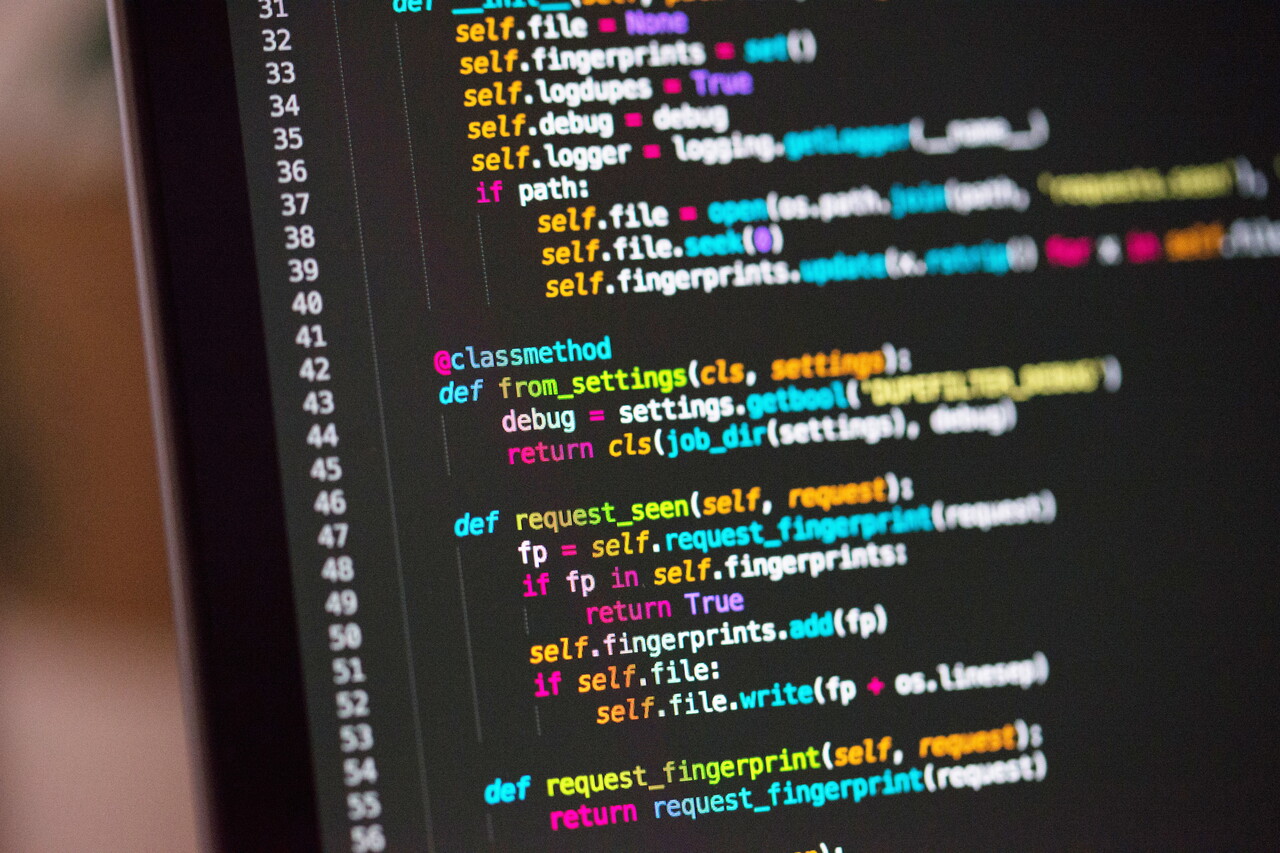 Schräg fotografierter Bildschirm mit farbig hervorgehobenem Programmcode auf dunklem Hintergrund, mit Zeilennummern am linken Rand.